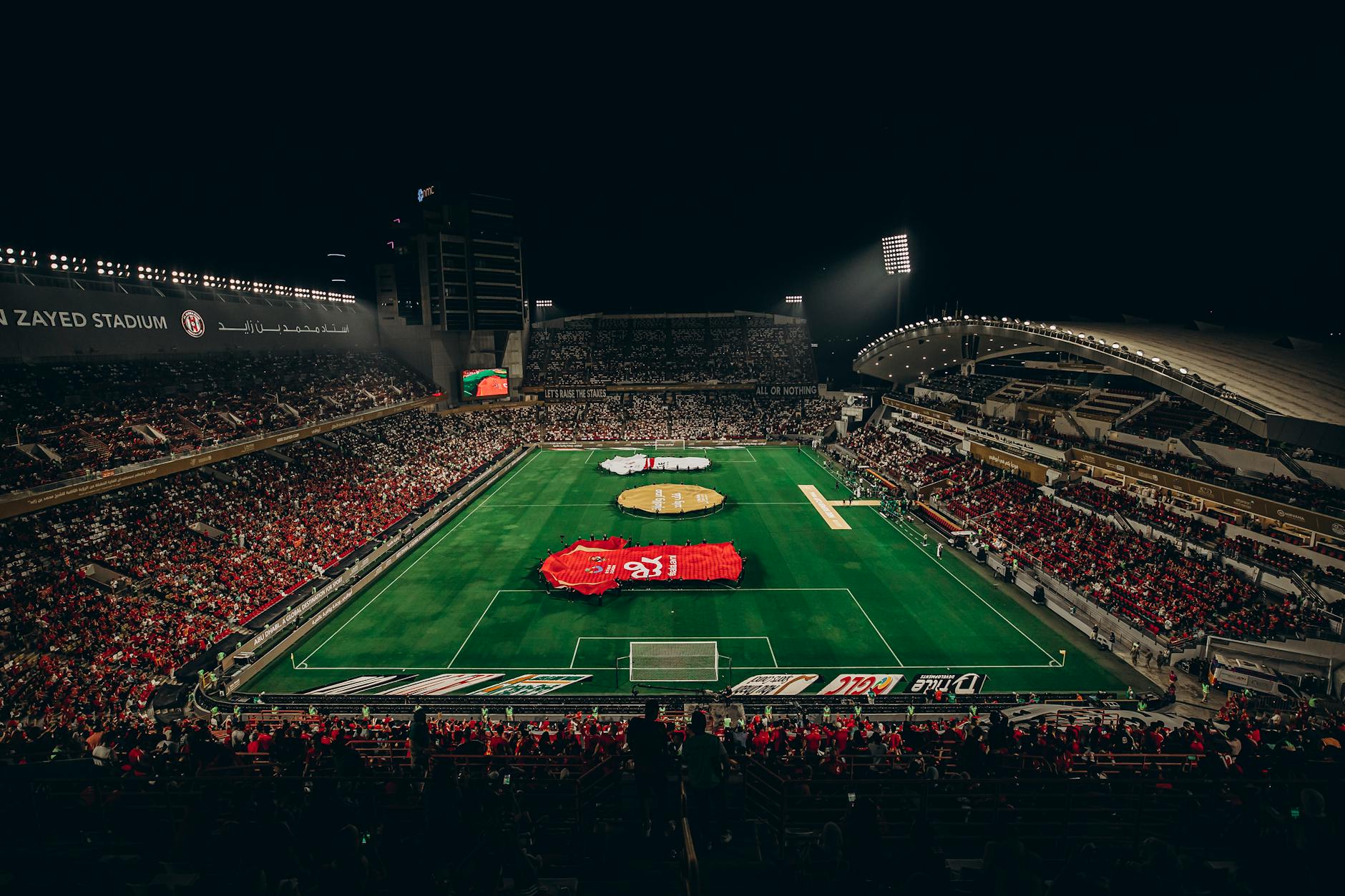 Aerial view of a lively football match at Zayed Stadium, showcasing fans and vibrant atmosphere.