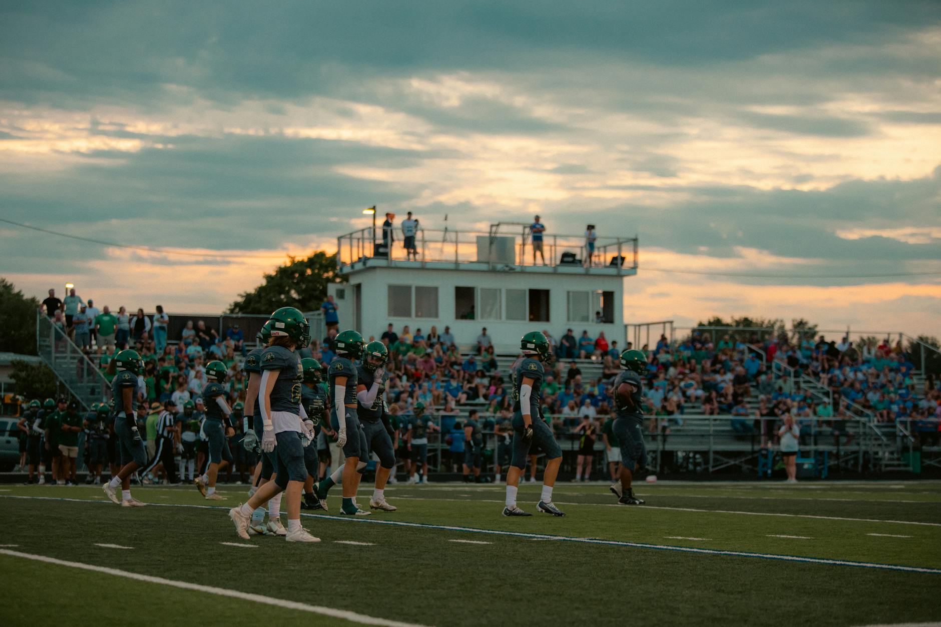 Football players and crowd in a stadium during a sunset game.